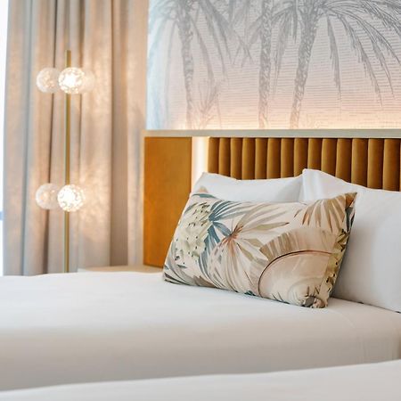 อโมรา บริสเบน Hotel ภายนอก รูปภาพ The photo shows a stylish hotel room featuring two neatly made beds with white linens. Each bed has several pillows, one of which has a decorative cover with a tropical plant pattern. Behind the beds is a modern headboard, and the wall is decorated w